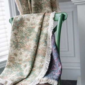 Green floral jacquard woven throw blanket with white fringe on a vintage wooden chair