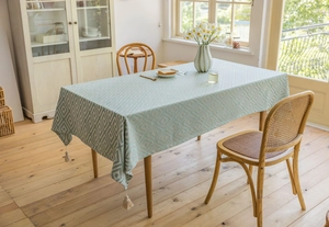 Detail of teal jacquard tablecloth with white geometric diamond patterns and tassel trim