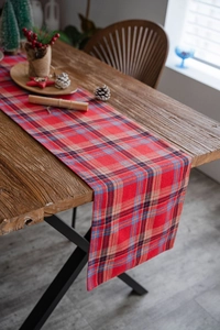 Detail of red and blue plaid table runner on a wooden table with festive pinecone decor