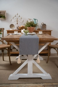 Close-up of blue and white striped table runner with cotton tassels on a wooden table