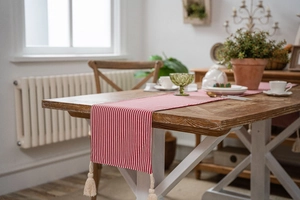 Detail of red and white striped table runner with elegant cream tassels on wooden table