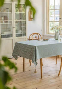 Detailed texture of green jacquard tablecloth featuring diamond pattern and beige tassels