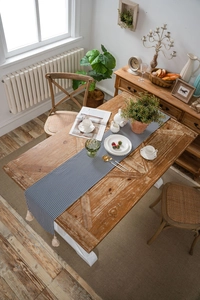 Close-up of blue and white striped table runner with white tassel fringe on wooden table
