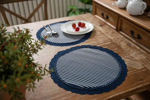 Close-up of blue and white striped round placemat with navy lace trim on a wood table