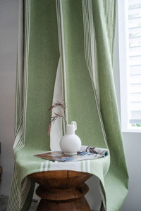 Detail of green and beige striped linen curtain draped over a wooden stool with natural texture
