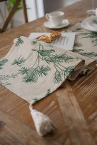 Close-up of linen table runner featuring green pine and bird prints with woven tassels