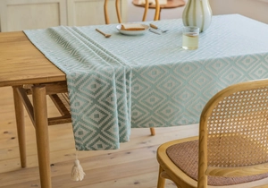 Detail of green geometric diamond jacquard tablecloth with fringe trim on wood table
