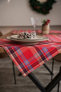 Detail of red plaid table runner with festive Christmas decor and rustic pine cones