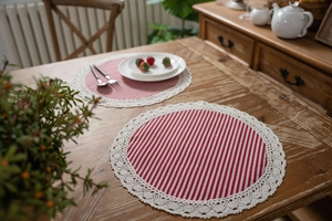 Close-up of circular cotton linen placemats with red white stripes and lace edges