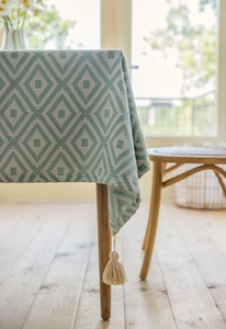 Detail of green jacquard geometric diamond tablecloth with delicate beige tassel accents
