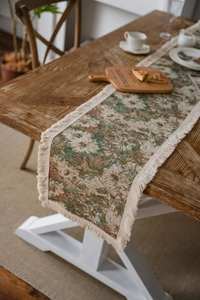 Dettaglio del runner da tavolo floreale vintage con nappe su tavolo in legno rustico
