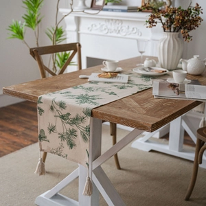 Floral table runner with pine needle prints and tassel edge on a dining table