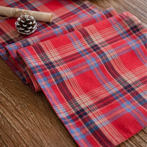 Red plaid table runner in rustic American style on a wooden surface with pine cones