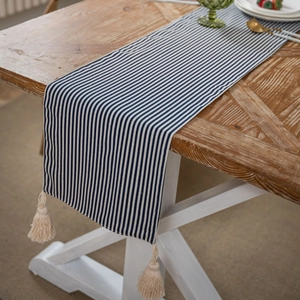 Modern blue and white striped table runner with cotton tassels on a wooden dining table