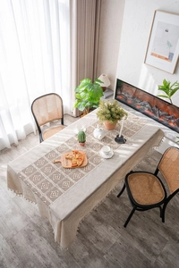 Detail showing beige hollow lace table runner with tassels on a rustic cotton linen cloth