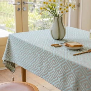 Green diamond patterned jacquard tablecloth with tassel fringe on a wooden dining table