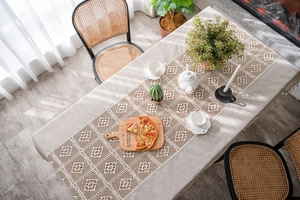 Close-up of beige knitted table runner with geometric hollow lace patterns on wooden table
