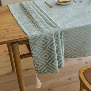 Mint green jacquard geometric table runner with cream tassels on a wooden dining table