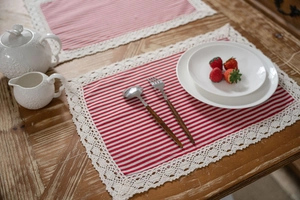 Dettaglio della tovaglietta a righe rosse con bordo in pizzo bianco su tavolo in legno