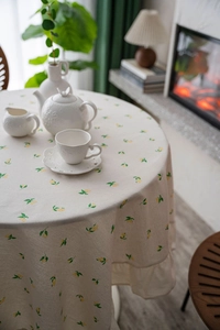 Detail of round beige tablecloth with mini lemon print and elegant ruffled edges