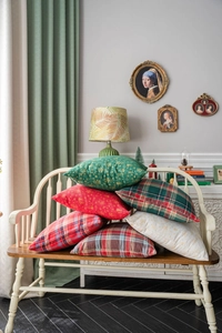 Classic green and red Christmas plaid pillow covers displayed on a vintage white bench