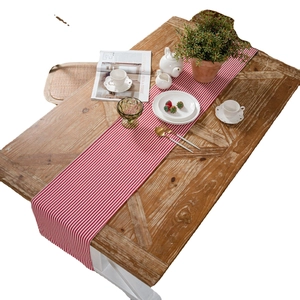 Farmhouse table runner with red and white thin stripes and tassels on wooden table