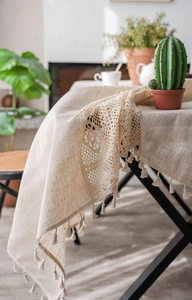 Close-up of beige linen tablecloth with hollow lace patchwork and fringe trim details