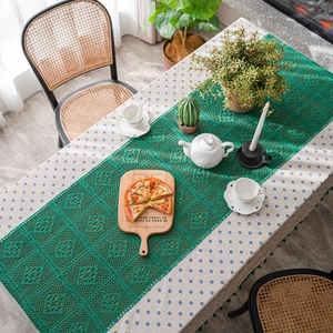 Dark green crochet table runner with hollow floral pattern and fringe over floral tablecloth