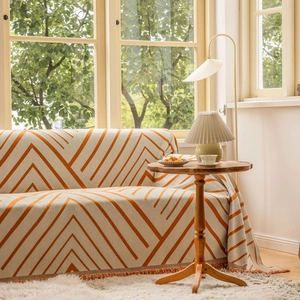 Thick geometric orange and cream sofa throw cover with decorative tassels in a modern living room