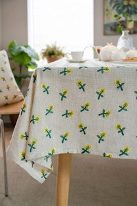 Detailed embroidery of small yellow daisies on a natural beige cotton linen tablecloth