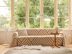 Close-up of orange and white V-stripe sofa cover with delicate fringe trim and soft pillow