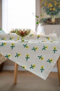Close-up of yellow floral embroidery on beige cotton linen tablecloth in warm home setting