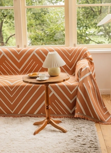 Close-up of thick orange geometric knit throw blanket with fringe tassels on a sofa