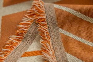 Close-up of geometric orange and beige knitted blanket with soft fringe detail