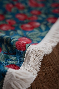 Macro detail of navy blue woven table runner with red cherry pattern and white tassels