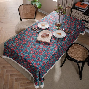 Navy blue tablecloth with red berry patterns and white tassels on a wooden dining table