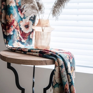 Floral woven jacquard blanket with fringes draped over a table in a bright room