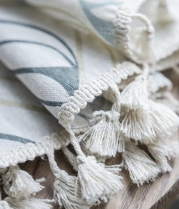 Detail of cotton linen fabric with tassels and abstract floral print on wooden background