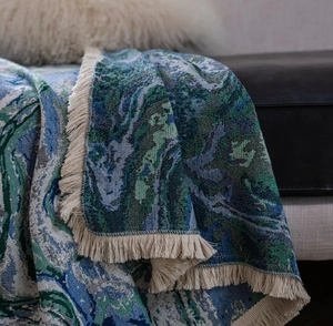 Detail of blue floral jacquard sofa throw with cream tassels on leather couch