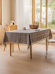 Close-up of dark brown cotton linen tablecloth with white stripes and cream fringe tassels