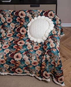 Close-up of vintage floral jacquard sofa throw with fringe details and a round white pillow