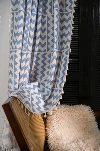 Détail de motifs géométriques bleus et franges blanches sur rideau en coton et lin