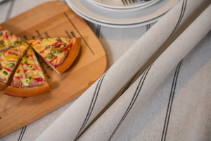 Detail of beige linen tablecloth with fine black stripes on a rustic wooden dining table