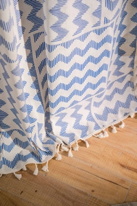 Vue détaillée du motif vagues géométriques bleues sur lin beige avec des pompons blancs