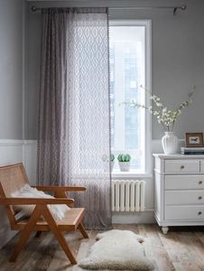 Close-up of grey crochet lace curtain with Damascus patterns and small pompom tassels