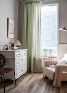 Détail d'un rideau en lin vert à rayures avec pompons beiges dans un salon moderne