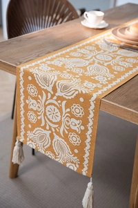 Close-up of orange jacquard table runner with white floral textures and tassels