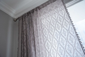 Detailed close-up of grey crochet lace curtain with geometric embroidery and tassel fringe