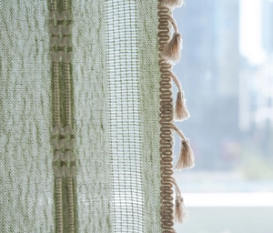 Gros plan sur rideau vert clair en maille ajourée avec bordure de franges beiges fines