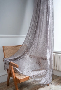 Detail of grey damask lace curtain with tassel fringe draped on a vintage rattan chair